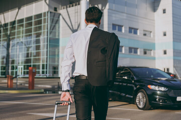Bottom back view young traveler businessman young man wearing black dinner suit walk go outside at international airport terminal with suitcase to car booking taxi Air flight business trip concept