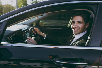 Side profile view young fun driver confident caucasian businessman man in black dinner suit driving...