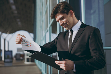 Satisfied young traveler businessman man in black classic tie suit standing outside at...