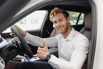 Man customer buyer businessman client in classic suit sit in car salon show thumb up chooses auto...