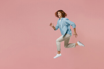 Fototapeta na wymiar Full length side view young runner sporty excited happy fun man 20s with long curly hair wear blue shirt white t-shirt run fast jump high isolated on pastel plain pink color wall background studio