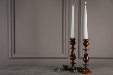Elegant candlesticks with burning candles and eucalyptus on grey table. Space for text