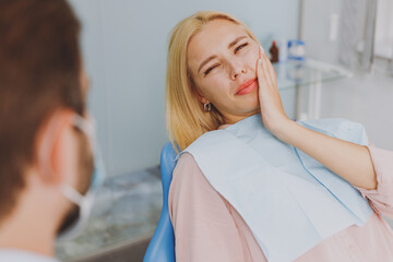 Young sad ill sick woman look at dentist sit at office chair indoor light cabinet hold cheeck...