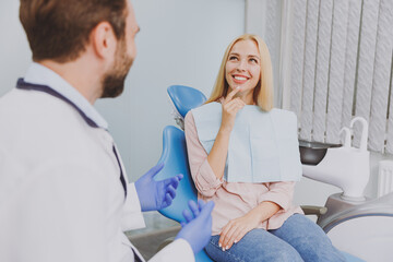 Young man dentist doctor in white gown talk speaking with patient consulting mindedwoman sit at...