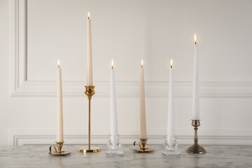 Elegant candlesticks with burning candles on white marble table - obrazy, fototapety, plakaty