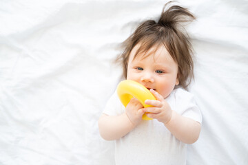 cute baby girl lying on bed and play with yellow plastic circle toy.