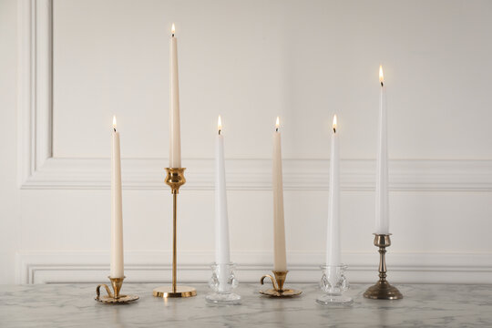 Elegant candlesticks with burning candles on white marble table