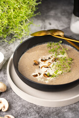 A mushroom soup with thyme, sour cream and fried champignons in a deep black bowl on a grey concrete surface