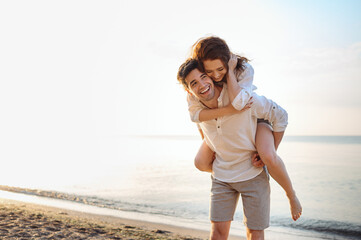 Young couple two friends family man woman in casual clothes boyfriend give piggyback ride to joyful, girlfriend sit on back at sunrise over sea beach ocean outside seaside in summer day sunset evening