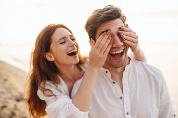 Young couple family man woman in white clothes rest together girlfriend meet boyfriend close eyes with hands play guess who or hide and seek at sunrise over sea beach outdoor seaside in summer day.