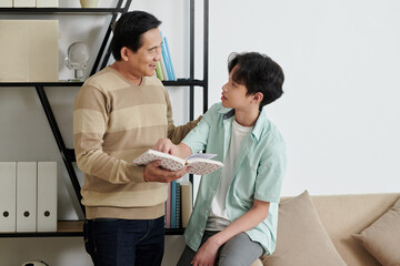 Positive father and son standing at shelf and discussing new book