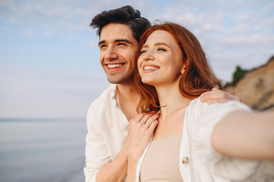Close up tender young couple two family man woman in casual clothes hug each other do selfie shot pov on mobile phone look aside at sunrise over sea beach outdoor seaside in summer day sunset evening.