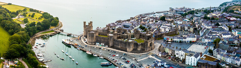 Aerial drone view of Caernarfon castle and battlements along the River Seiont in North Wales - obrazy, fototapety, plakaty