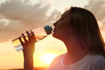 Young woman drinking water to prevent heat stroke outdoors at sunset