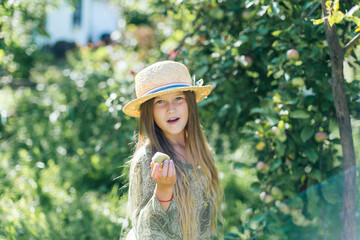 девочка смеется , кушает яблоки в соломенной шляпе 