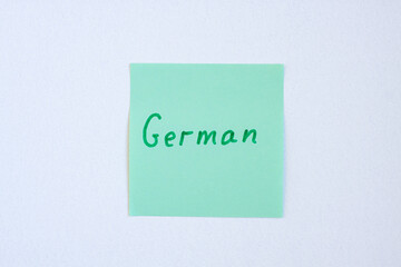 Top view flat lay of the reminder notepaper of green color with word German on it on white background. Flashcards and language studies concept