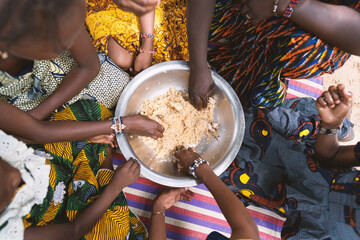 Group of black African girls sitting in a circle around a large plate of cereals, eating their meager vegan meal together with their hands