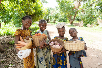Group of pretty smiling African girls carrying baskets full of vegetables, on their way to the lokal market - obrazy, fototapety, plakaty