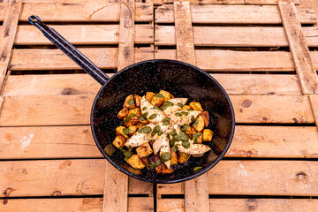 Country frying pan with fried chicken breasts and fried diced potatoes with Italian pesto sauce on wooden boxes