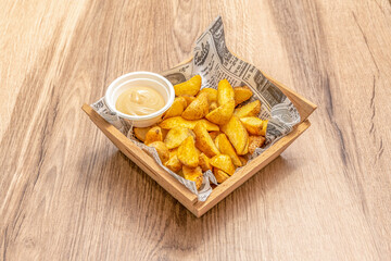 Portion of French fries with skin in a wooden bowl with a bowl of sauce for dipping
