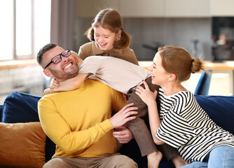 Happy beautiful family having fun and playing while relaxing on sofa in living room