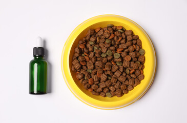 Glass bottle of tincture near dry pet food in bowl on white background, top view
