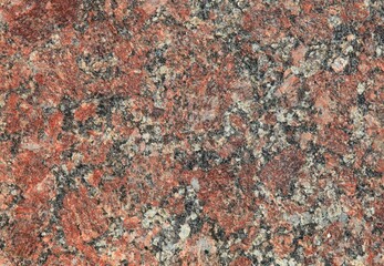Red granite texture. A variegated, spotted background of red (brown) granite. The stone granite surface of brown-gray color. Surface view of granular igneous rock