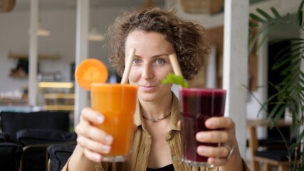 Blonde girl showing to the camera glasses of natural organic carrot and beetroot juices with paper straws. Plant based cold refreshing drinks.