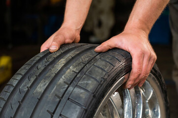 Obraz premium auto mechanic holds a wheel of a car. Change of car tires acc