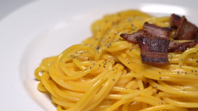 Spaghetti with carbonara, traditional pasta dish of Italian culture made with fresh egg yolk, original grated pecorino romano, crispy bacon and black pepper.