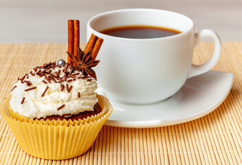 Cup of coffee and cupcake with cream and decorative chocolate sprinkles, cinnamon and anise
