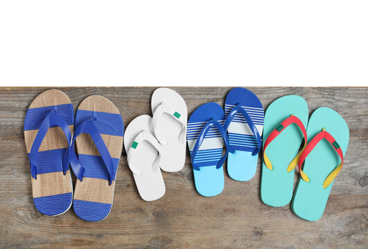 Pairs of bright flip flops on wooden table against white background, top view