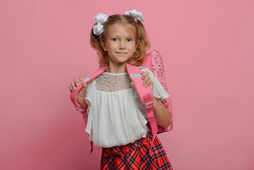 Elementary school girl carries a backpack. Isolated on pink background