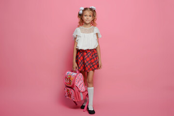 Elementary school girl carries a backpack. Isolated on pink background