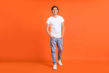 Fototapeta na wymiar Full body photo of young happy man walk hands pockets jeans isolated on shine orange color background