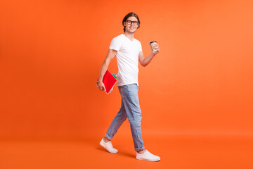 Fototapeta na wymiar Full body photo of young attractive happy man walk empty space hold note coffee isolated on orange color background