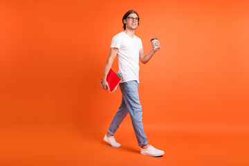 Fototapeta na wymiar Full length photo of young dreamy happy man look go empty space hold note coffee isolated on orange color background