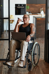 Full length portrait of contemporary tattooed woman with disability using laptop and smartphone while working from home