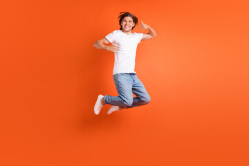 Full length photo of young happy positive man jump up make thumb up smile isolated on orange color...