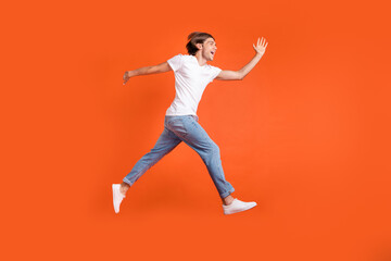 Fototapeta na wymiar Full size profile side photo of happy young cheerful crazy man jump run empty space isolated on orange color background