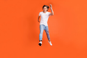 Fototapeta na wymiar Full body photo of positive young happy man jump up runner dream travel isolated on orange color background
