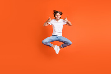 Fototapeta na wymiar Full length photo of young funky happy man jump up good mood thumbs up isolated on orange color background