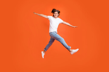 Full body photo of cheerful young happy positive man jump up hands plane wings isolated on orange color background