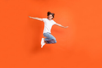 Full length photo of young happy funky man jump up air hands wings plane smile isolated on orange color background
