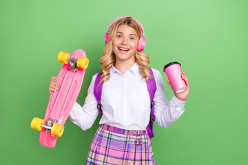 Obraz premium Portrait of attractive cheerful girl listening hit drinking cappuccino holding skate isolated over green color background