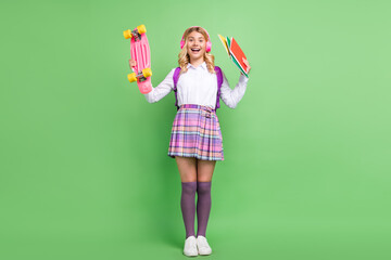 Full length body size view of attractive cheerful girl listening hit holding skate book isolated over green color background