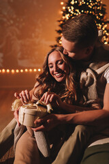 The concept of Christmas. A happy man and a woman in love celebrate the winter New Year holidays at night in a cozy house. A couple in love are kissing hugging together watching a movie eating popcorn