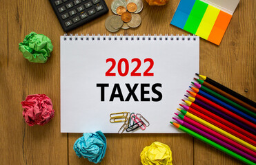 2022 taxes new year symbol. White note with words 2022 taxes on beautiful wooden table, colored paper, colored pencils, paper clips, coins and calculator. Business and 2022 taxes new year concept.