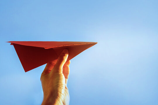 Hand holding red paper airplane with blue sky 