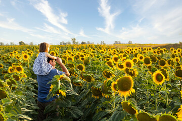 A father with a little daughter on his shoulders walk and have fun in the field of sunflowers. Close-up. Place for your text.